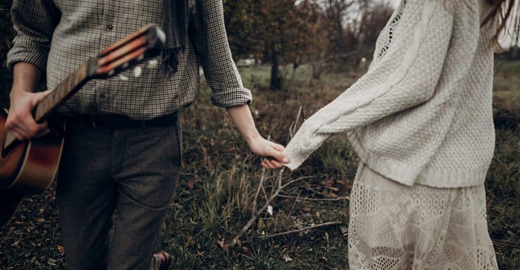 A man holding a guitar and a woman holding his hand, walking outdoors.