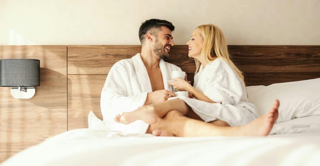 A couple in bathrobes enjoying coffee in bed.
