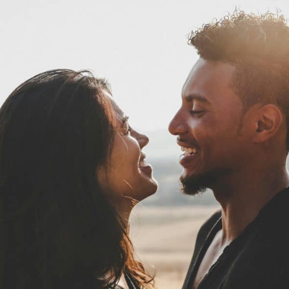 A man and woman laughing with each other, bathed in sunlight outdoors.