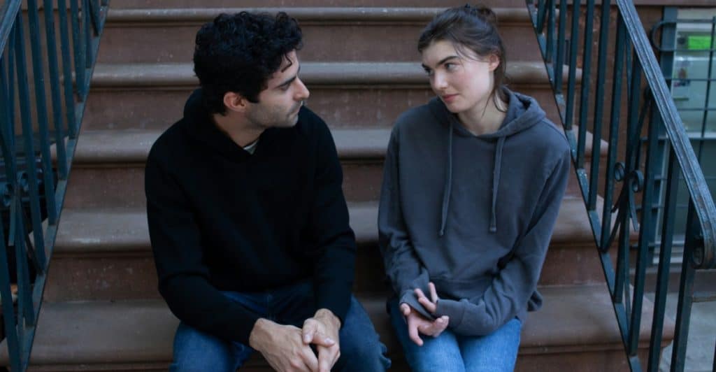 A man and a woman sitting on outdoor stairs, looking at each other.