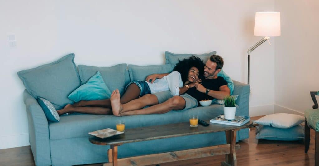 A couple relaxing on a light blue couch, with the woman resting her head on the man's chest.