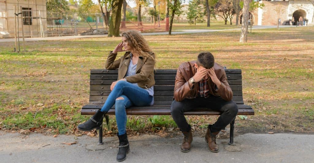 A man and a woman sitting apart on a park bench, both looking away from each other.