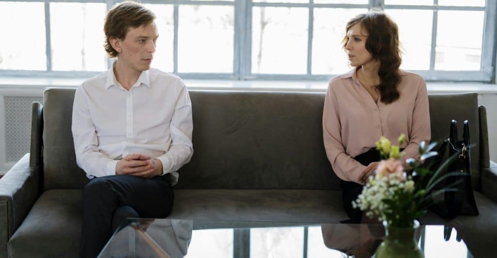 A man and a woman sitting at opposite ends of a couch, looking in different directions.