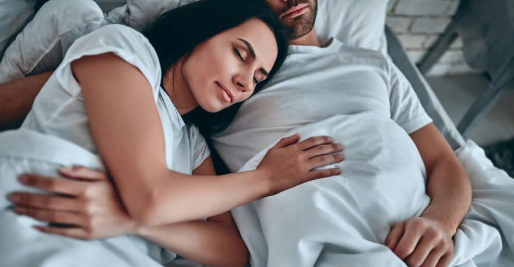 A man and a woman sleeping closely embraced in bed under white covers