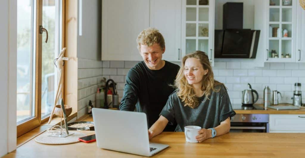 A man and a woman smiling while looking at a laptop together in a modern kitchen