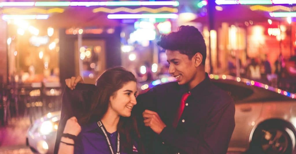 A young couple smiling and looking at each other on a city street at night.
