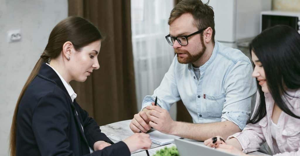 A couple sitting at a table across from another person, who appears to be an advisor, all looking at documents and talking.