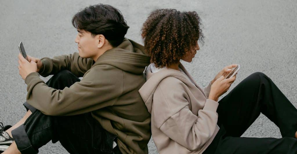 A couple sits side by side watching screens but not engaging with each other, illustrating passive detachment from the relationship.