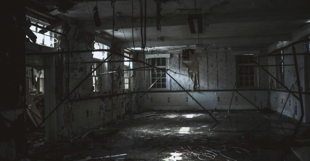 A dark, ruined room with debris on the floor and exposed beams.