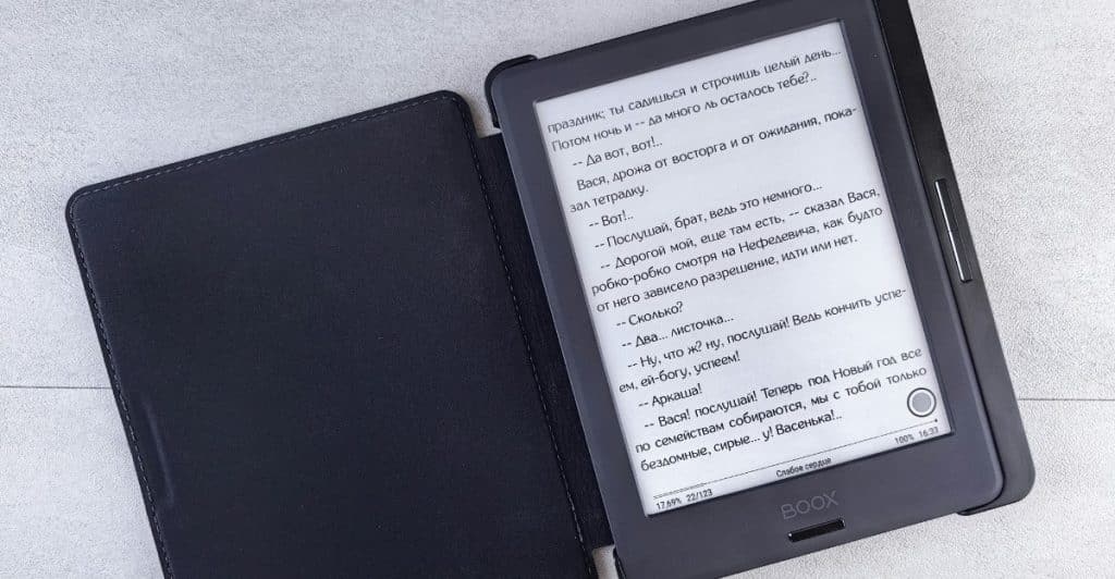 An E-Ink tablet displaying text, with its black cover open on a gray surface.