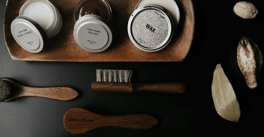 An overhead shot of wooden grooming brushes and tins of wax and polish on a wooden tray and dark surface.
