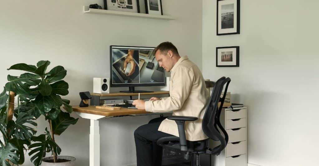 A modern office setup with a gray ergonomic chair, an adjustable standing desk, and two computer monitors, designed for comfortable and healthy work.