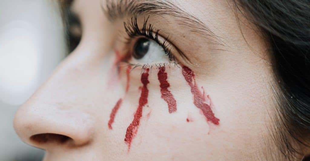 A close-up of an eye with red, blood-like streaks running down from it.