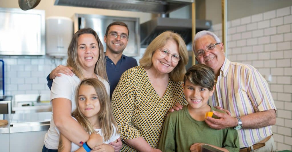 A multi-generational family, including children and adults, smiling and posing together in a kitchen.