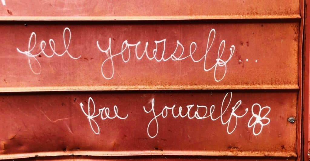 White cursive text on a reddish-brown corrugated metal surface, reading "feel yourself..." above "free yourself".