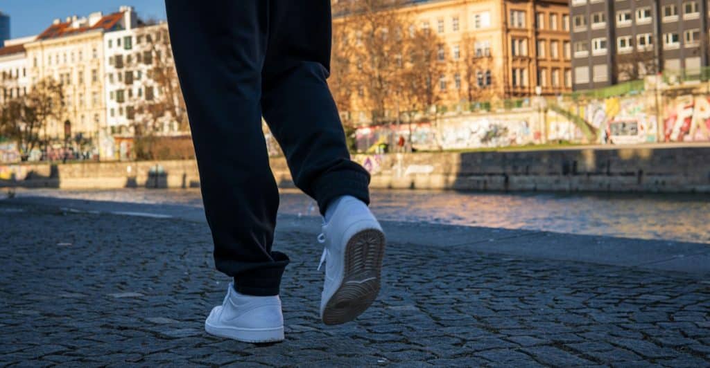 A person walking by a river in white sneakers.
