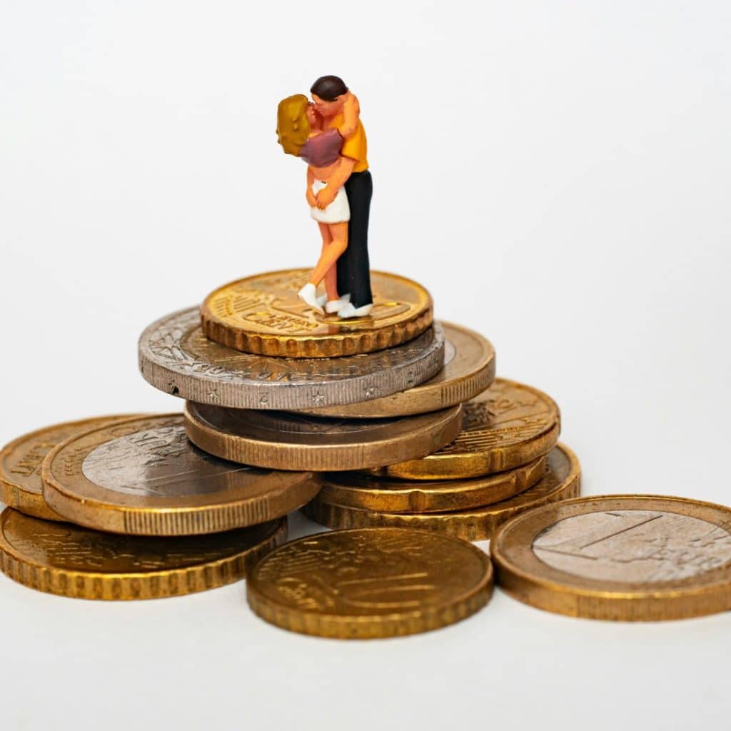 Two small figurines of a couple kissing, standing on a stack of various coins.