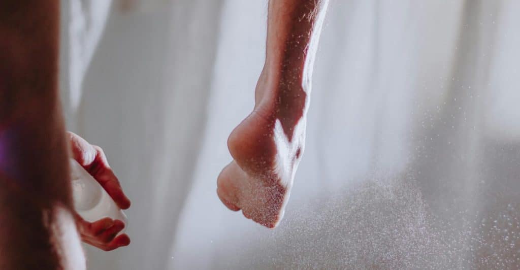 A close-up of a person's foot as white powder is sprayed onto it, with a hand visible holding the spray.
