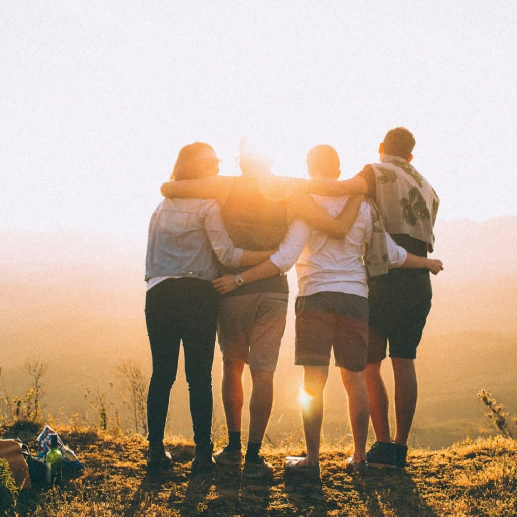 Four friends embracing and looking out at the sunset over mountains