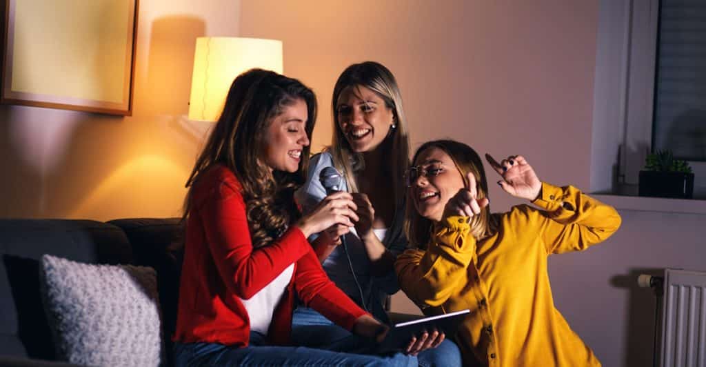 Three women cheerfully singing karaoke on a couch.