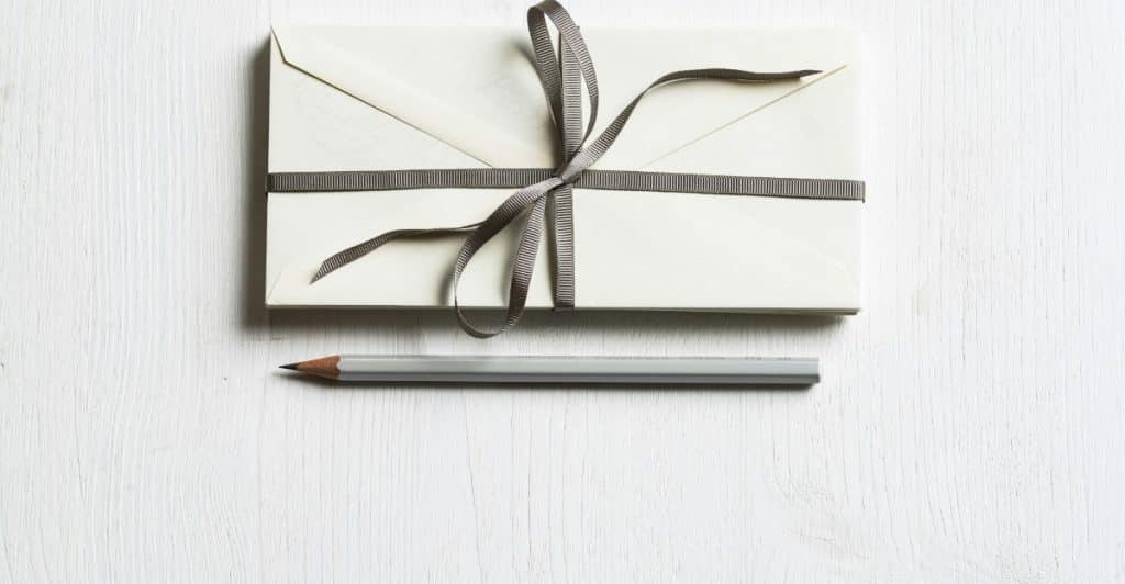 A small, flat gift wrapped with ribbon, next to a pencil on a white surface.