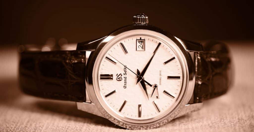 A close-up of a Grand Seiko watch with a white dial, a date window, and a brown leather strap.