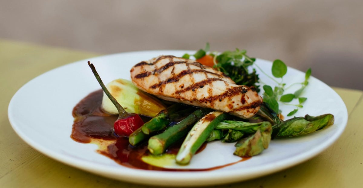 A grilled chicken breast with vegetables and a sauce on a white plate.