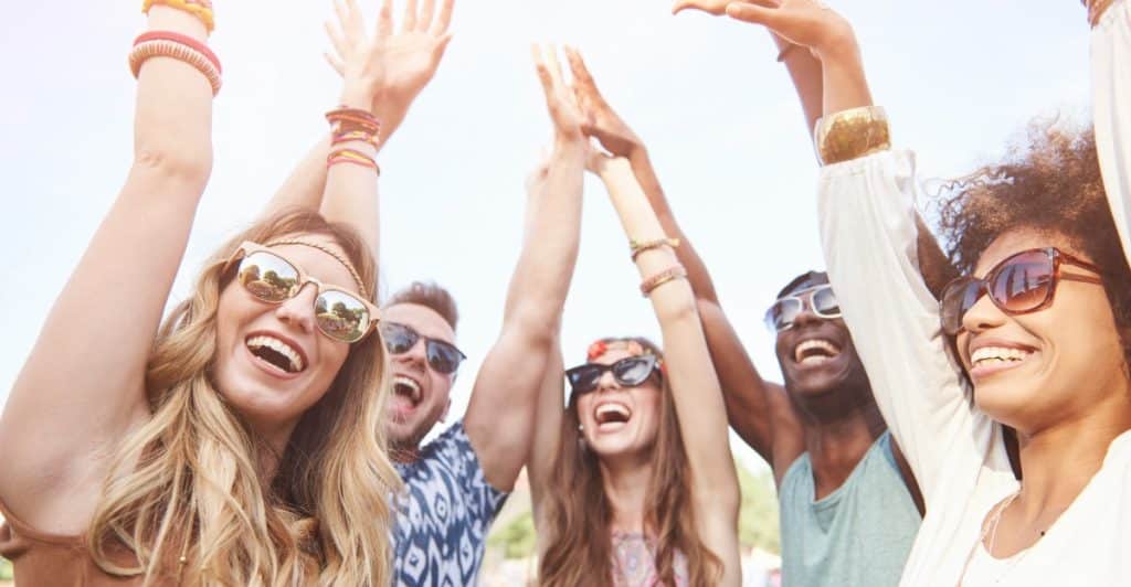 A group of diverse friends with their hands raised in the air, cheering and smiling.