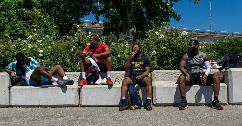 A group of four men resting and drinking water outdoors in an urban setting.