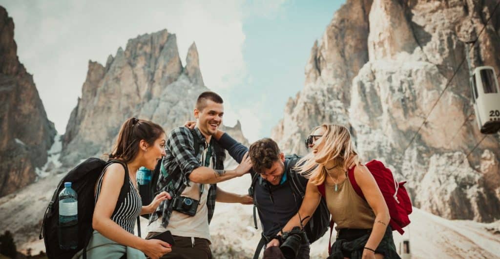  A group of four friends laughing and playfully interacting in a mountainous outdoor setting.