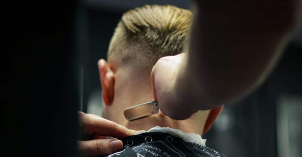 A barber using a straight razor to trim the hair on the back of a client's neck.