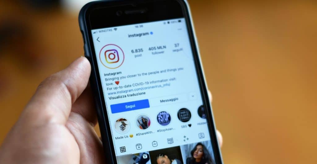 A close-up of a hand holding a smartphone showing an Instagram profile.