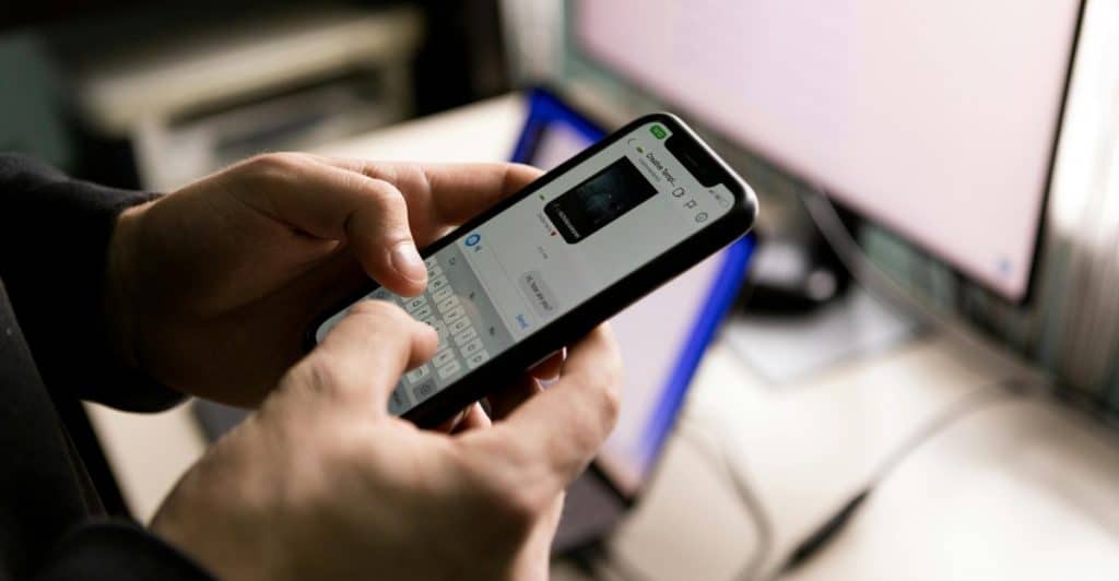 A person's hands typing on a smartphone.