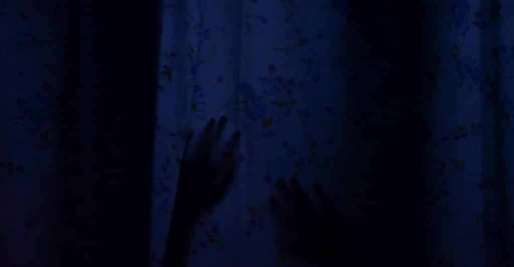 Two silhouetted hands pressing against a blue patterned curtain in the dark.