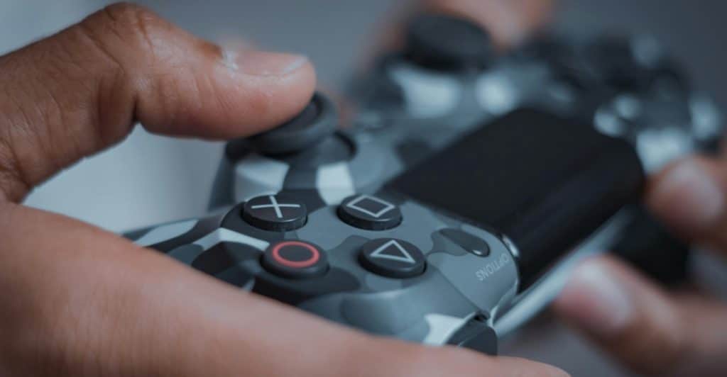 A person's hands are shown holding a camouflaged game controller with their thumbs resting on the joysticks.