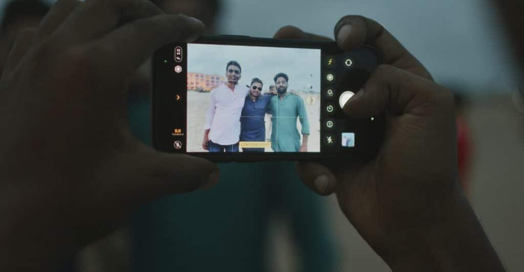 A person's hands holding a smartphone, capturing a photo of three men standing outdoors