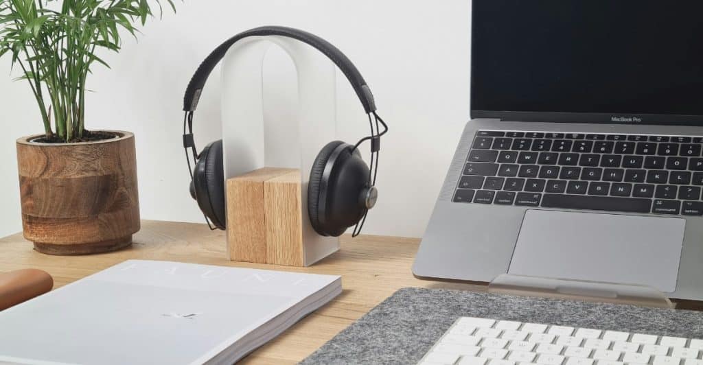 Black over-ear headphones on a wooden stand next to a laptop and a small plant on a desk