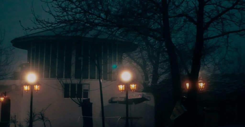 A house in a foggy, dark forest illuminated by several lanterns