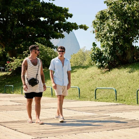 Two men walking and chatting on a wooden boardwalk beside a grassy park.