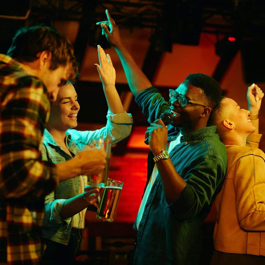 A diverse group of friends singing karaoke with drinks.