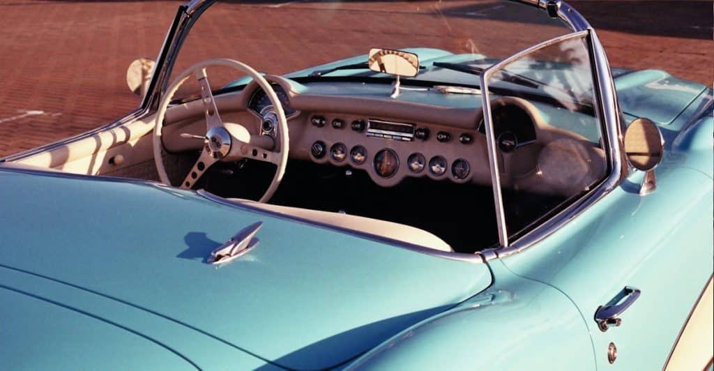 The interior and front hood of a light blue vintage convertible car with a tan dashboard.