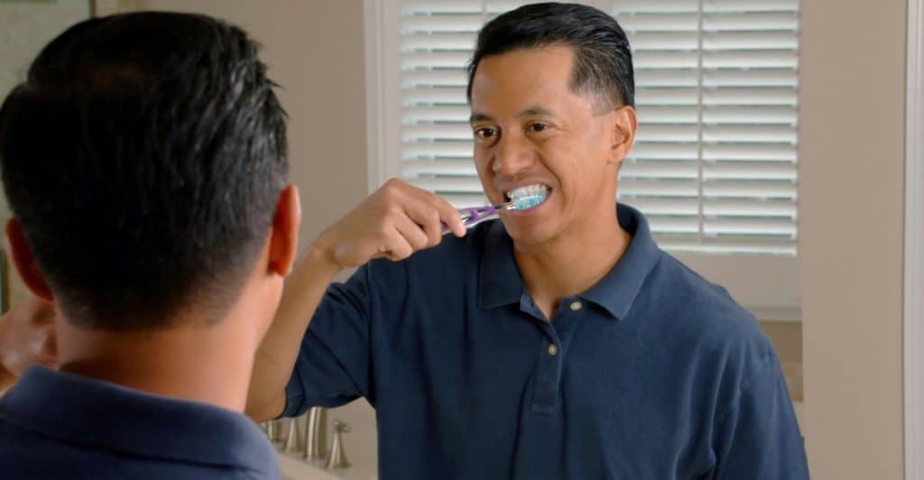 A man brushing his teeth while looking in a mirror.