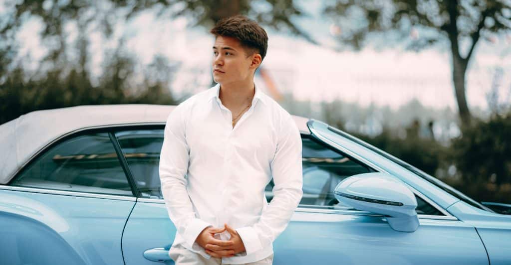 A man in a white shirt standing next to a blue convertible car.