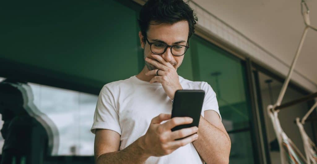 A man with glasses looking at his phone with a surprised or concerned expression.