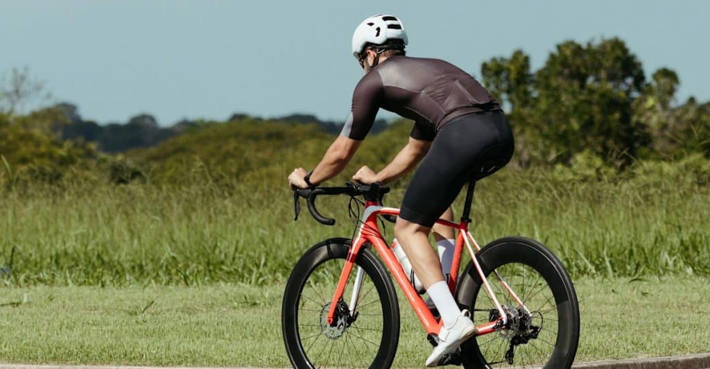 A man riding a road bicycle on a paved path with grassy fields on either side.