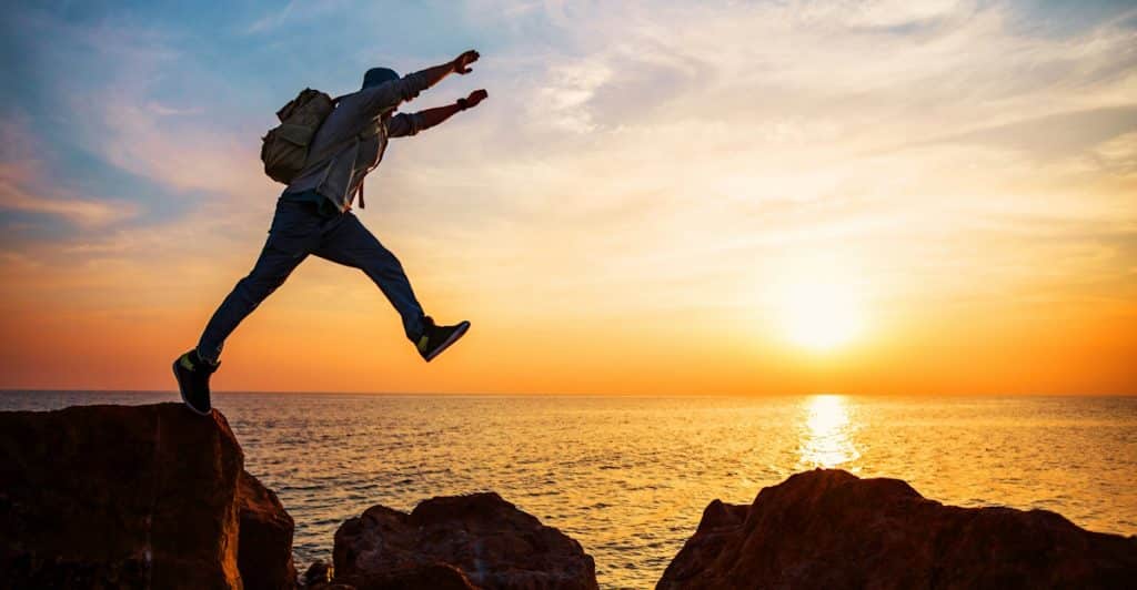 A man jumping over rocks near a body of water.
