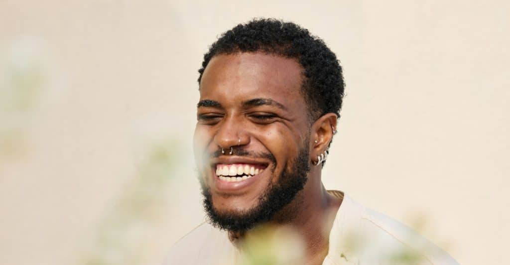 A smiling man with facial piercings and a light shirt.