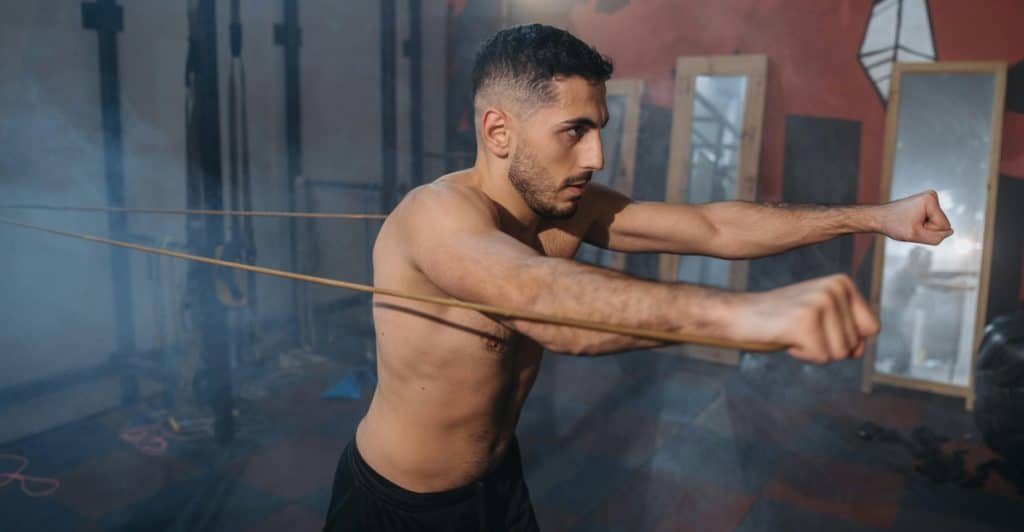 A shirtless man using a resistance band in an indoor gym setting.