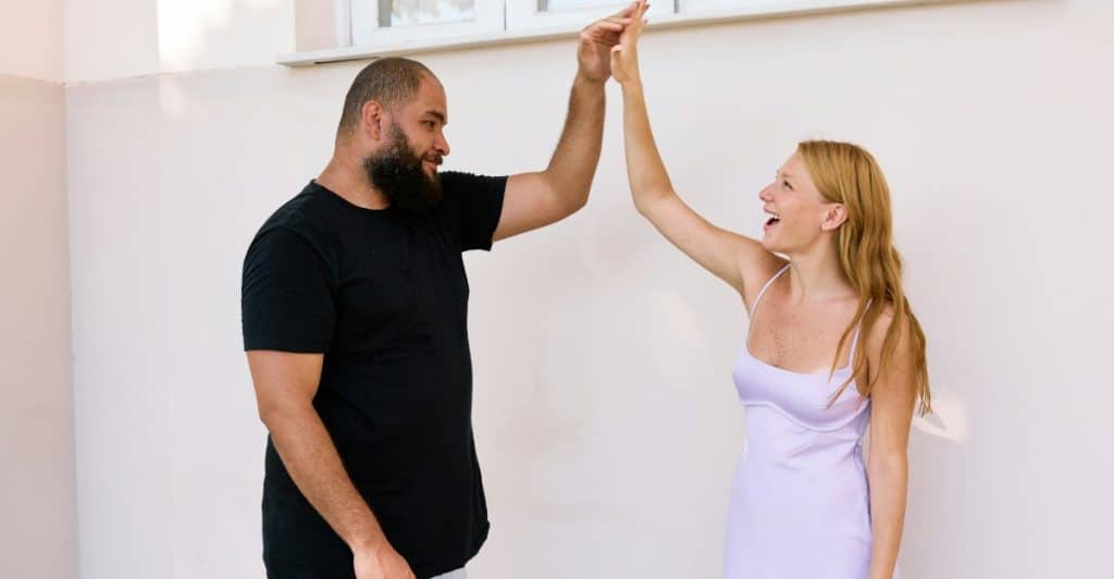 A man with a beard and a woman with long blonde hair are high-fiving each other outdoors.