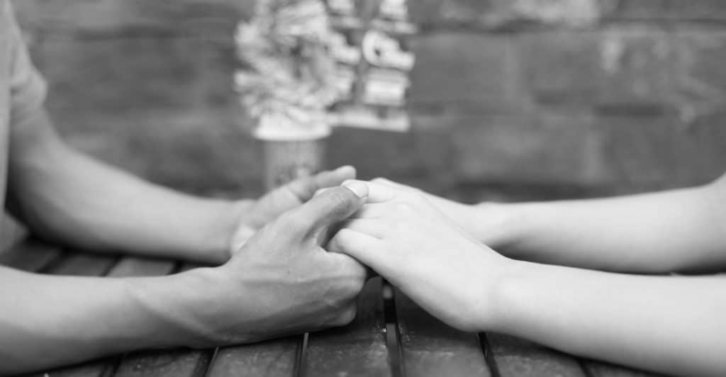 A man and a woman holding hands across a table with a coffee cup in the background.